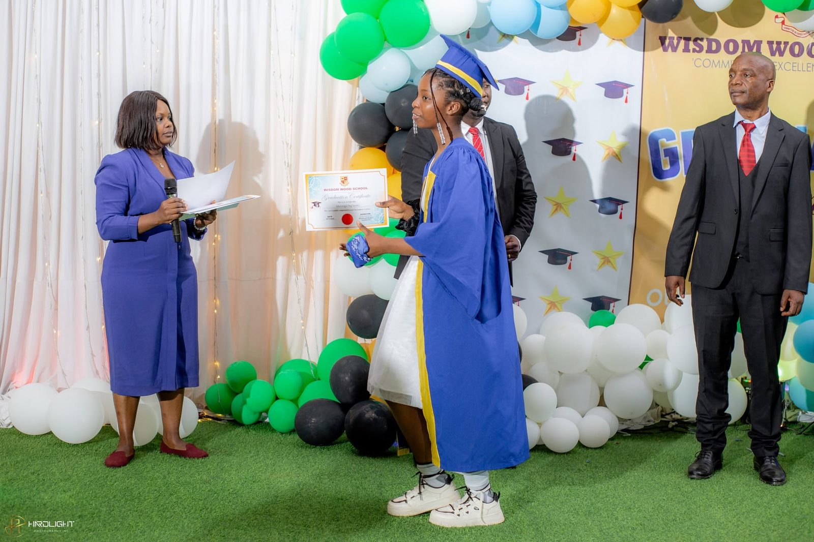 A graduate receiving her certificate in front of the Wisdom Wood School backdrop